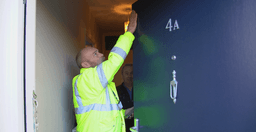 Technician performing maintenance on a multiperformance flat entrance doorset to ensure compliance and functionality
